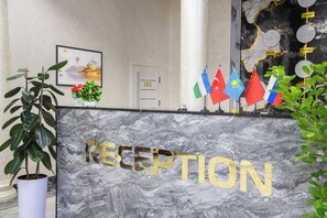 A reception desk with a marble countertop and the word 'RECEPTION' in gold letters. Flags of various countries are displayed on the wall behind the desk. - Art hommee (TASHKENT)