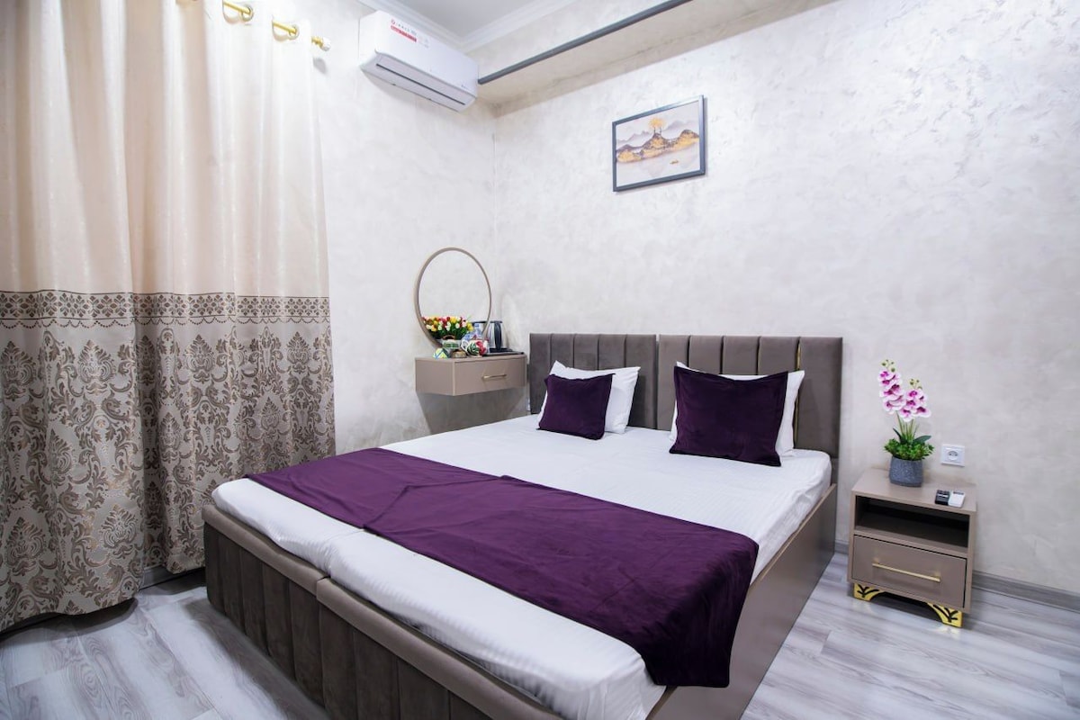 A bedroom with a bed, a nightstand, a mirror, and a wall-mounted air conditioner.