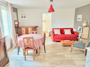 A cozy living room with a red sofa, wooden dining table, and chairs. - Apartment 'Studio Cozy à pied de la Plage' with Wi-Fi (Guilvinec)