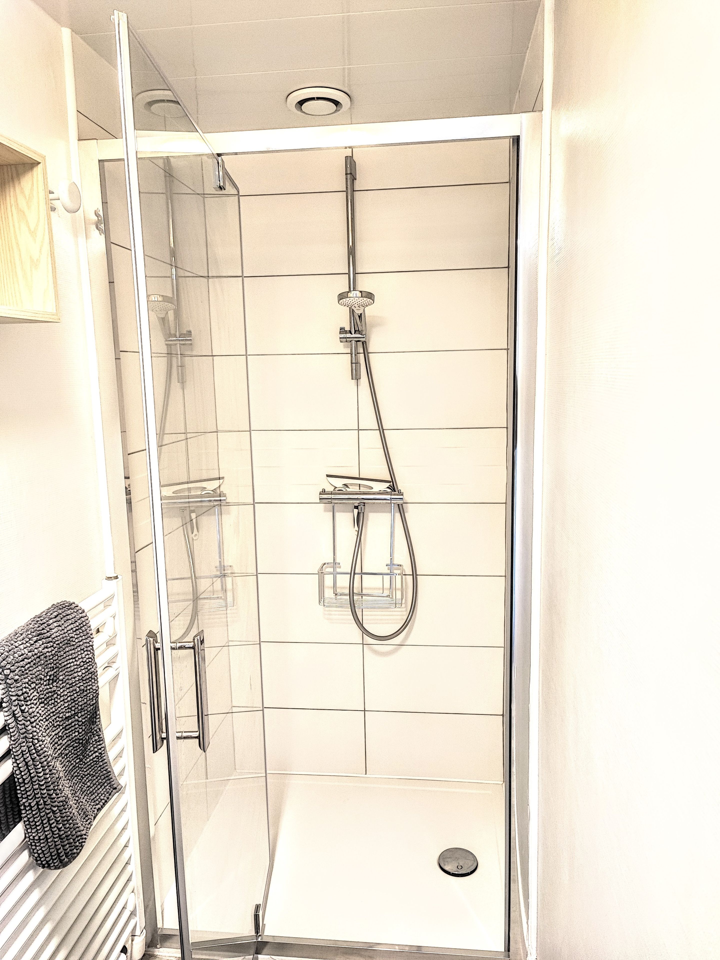 Una cabina doccia in vetro con soffione a mano e rubinetto a parete.