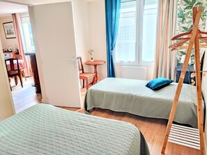 Ett rum med två sängar, en trästege, ett litet bord med en stol och ett fönster med gardiner.