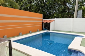 Et rektangulært swimmingpool med flisekant, omgivet af en hvid mur og et afsnit med orange og hvide striber.