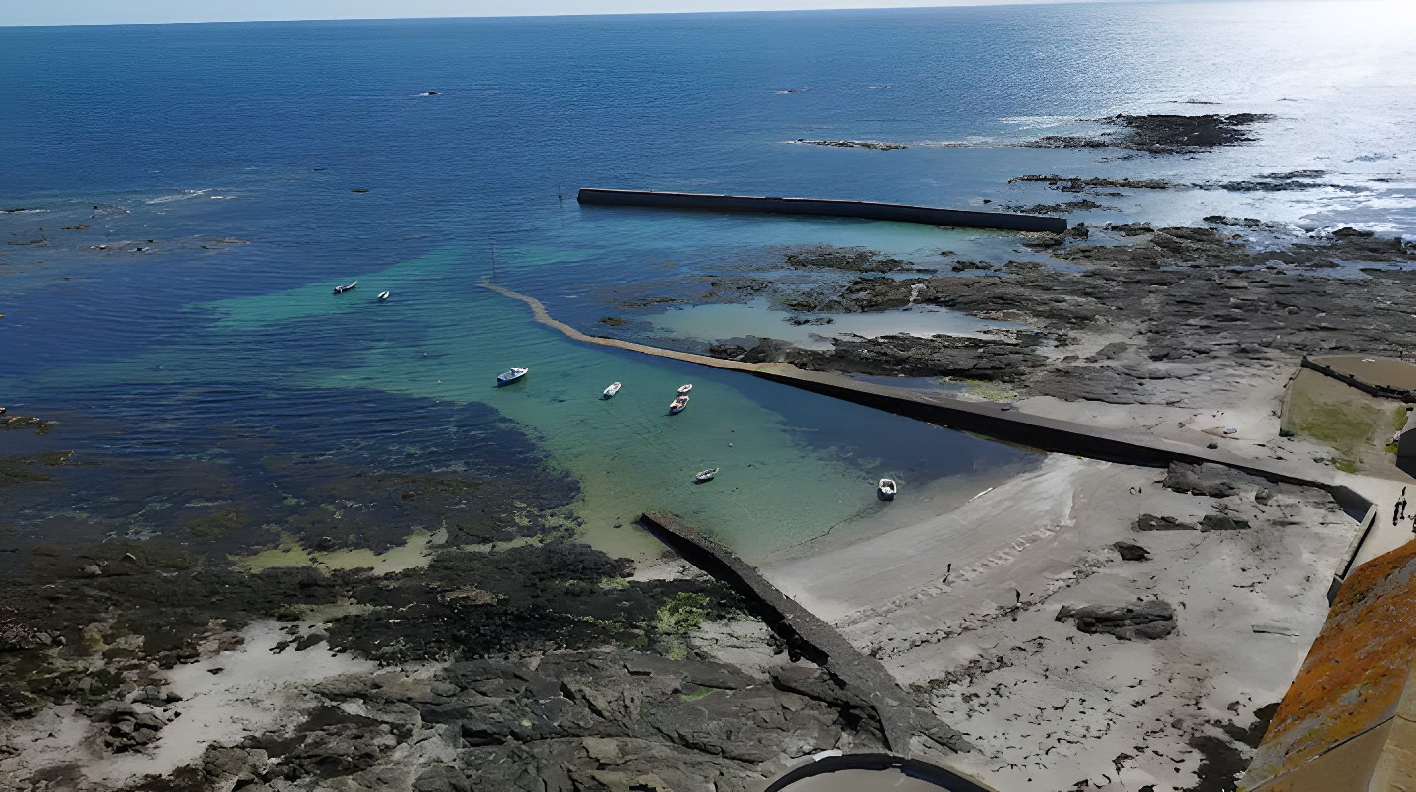 Eine Küstenlandschaft mit klarem Wasser, Booten und felsigem Gelände.