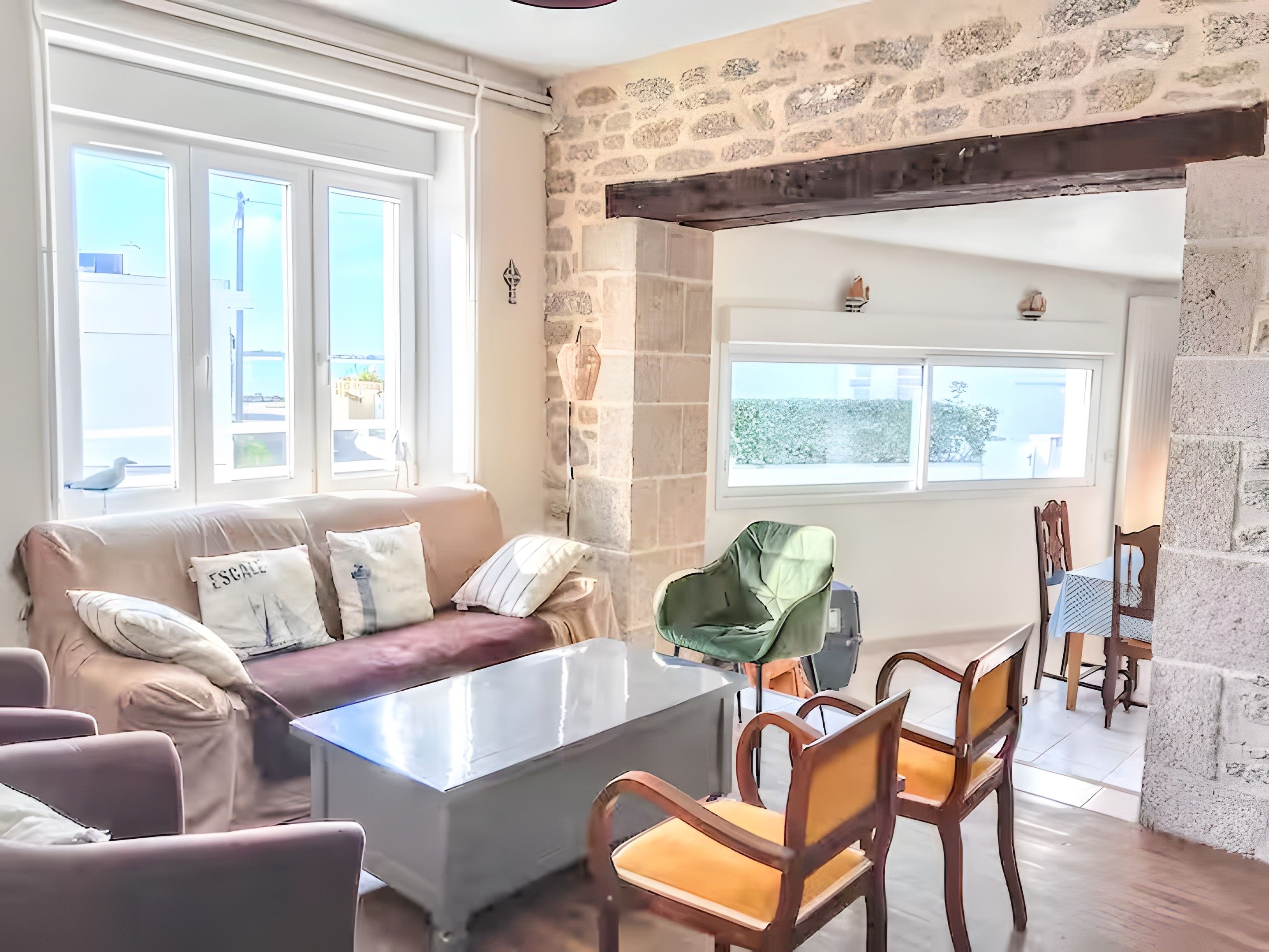 A cozy living room with a stone wall, a sofa with cushions, a coffee table, and a dining area with chairs and a table.