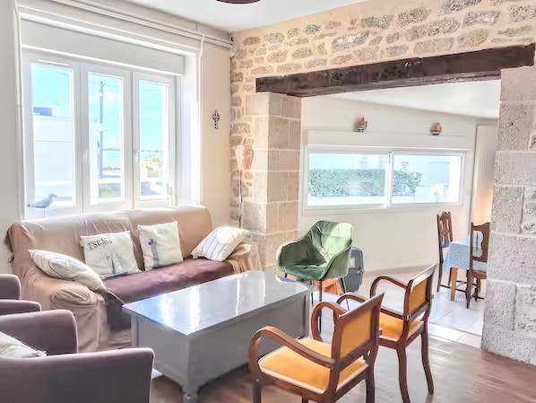 A cozy living room with a stone wall, a sofa with cushions, a coffee table, and a dining area with chairs and a table.