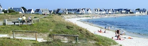 A beach with a wooden walkway, people sunbathing, and houses in the background.