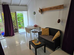Une pièce comprenant une table à manger, un canapé, une petite table avec un plateau et un ventilateur.