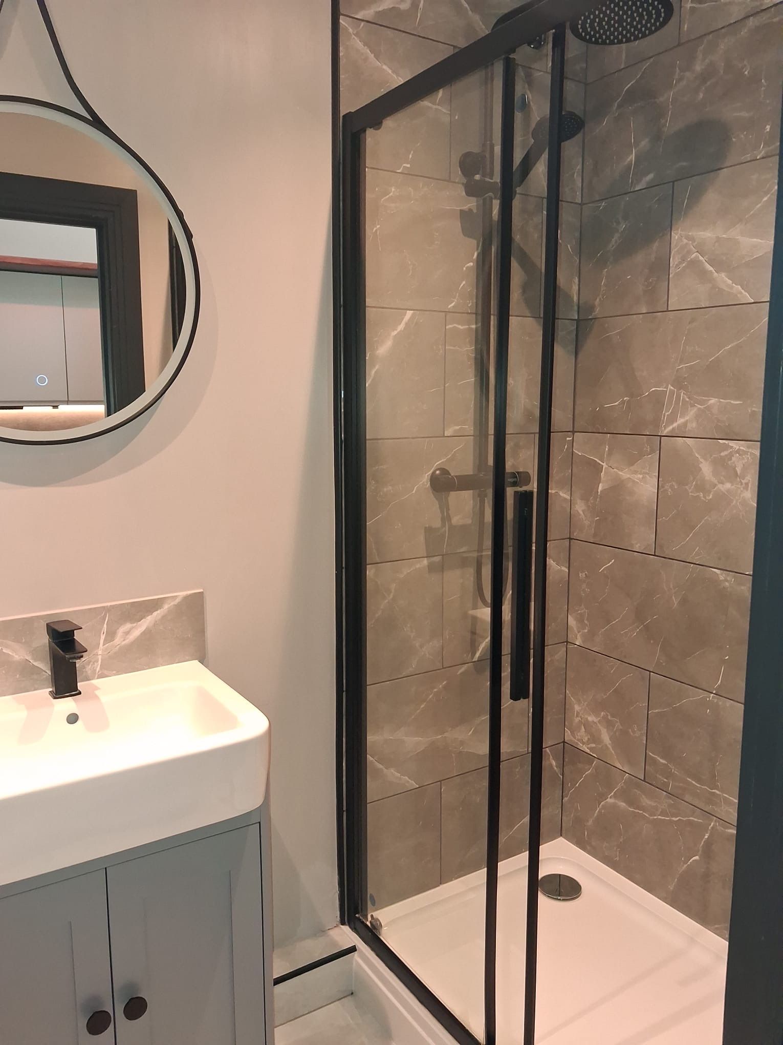 Ein modernes Badezimmer mit einer Glaskabine zur Dusche, einem weißen Waschbecken und einer Wand mit Marmorplatten.