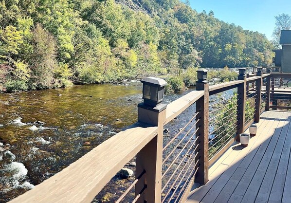 A wooden deck with a railing overlooking a river, surrounded by trees.