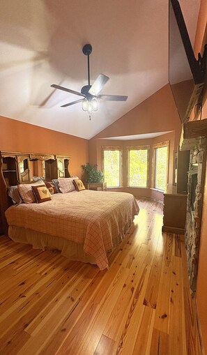A bedroom with a large bed, a ceiling fan, and a stone fireplace.