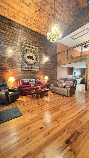 A spacious living room with a wooden ceiling, a large rug, and two leather sofas.