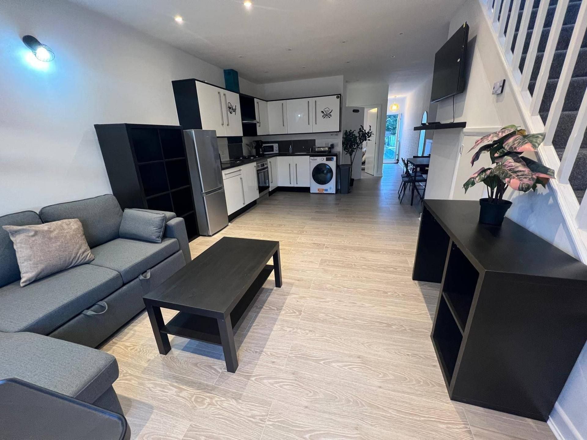 Een moderne woonkamer met een grijze bank, een zwarte salontafel, en een keuken met witte kasten en apparatuur.