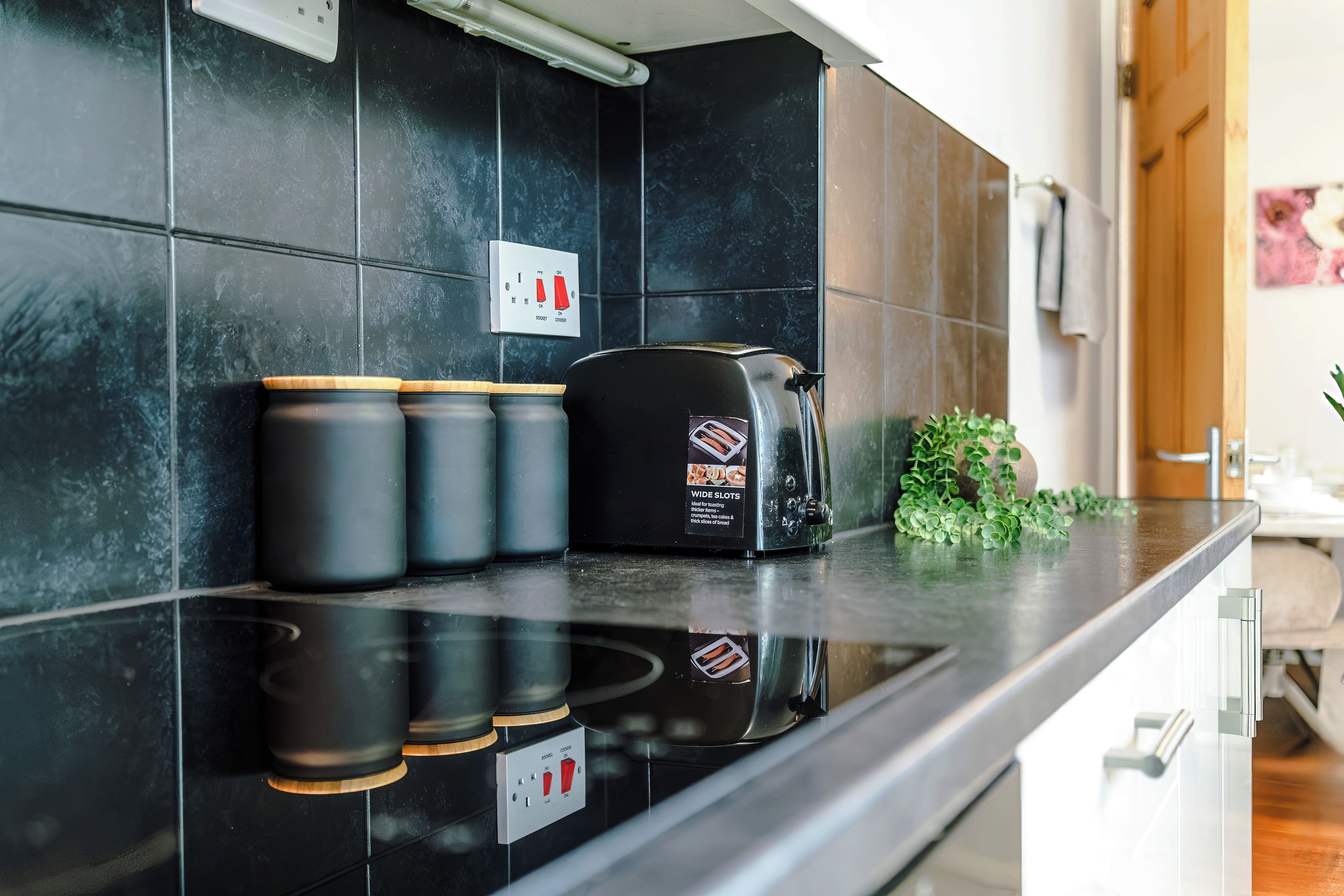 A kitchen with a black countertop, a toaster, and three black containers.