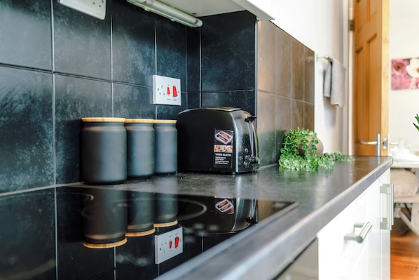 A kitchen with a black countertop, a toaster, and three black containers. - 3-Bed Home, Garden & Driveway, Sleeps 6 (Knutsford)