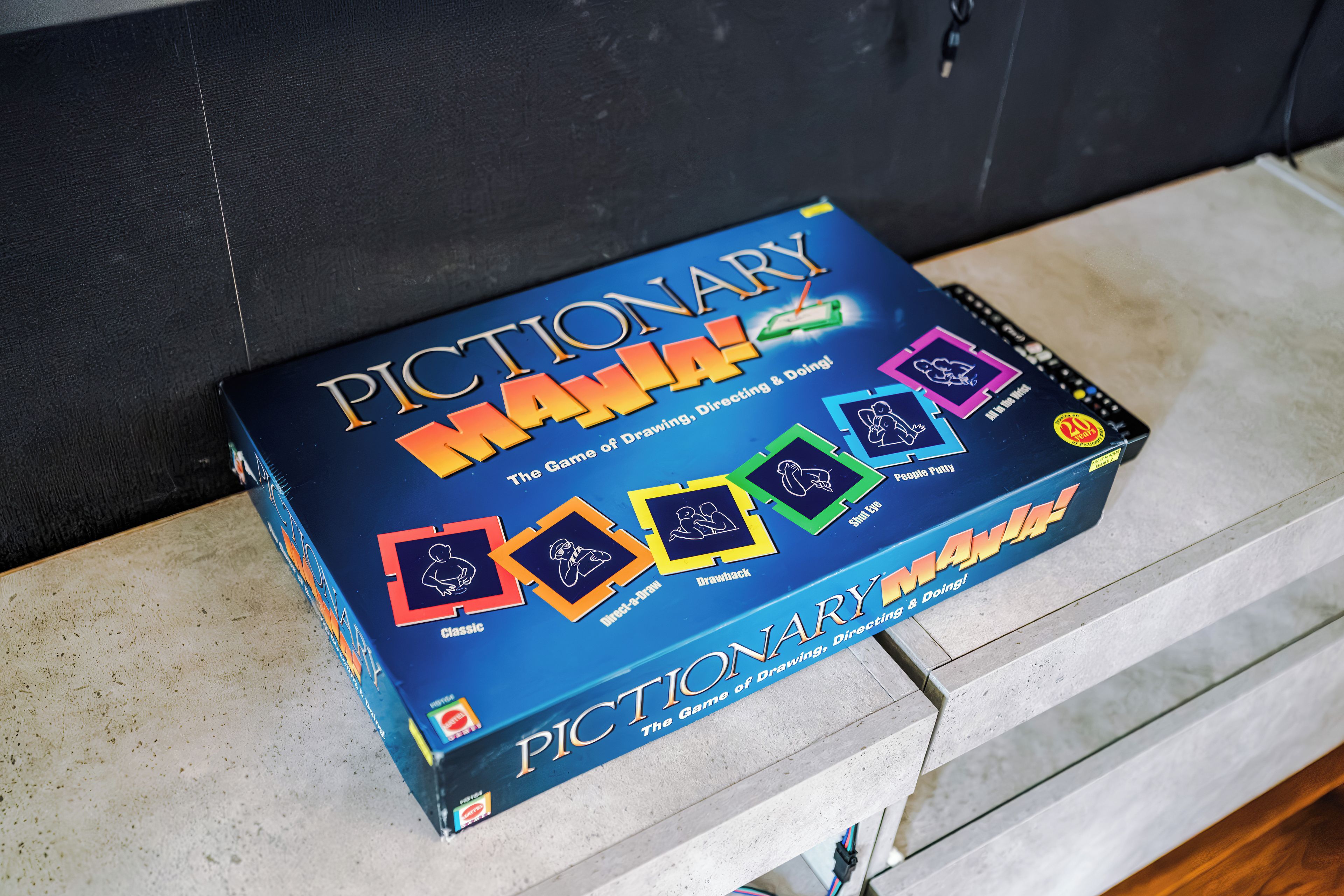 Una caja de juego titulada 'Pictionary Mania!' con diferentes modos de juego y una celebración por su 20 aniversario.