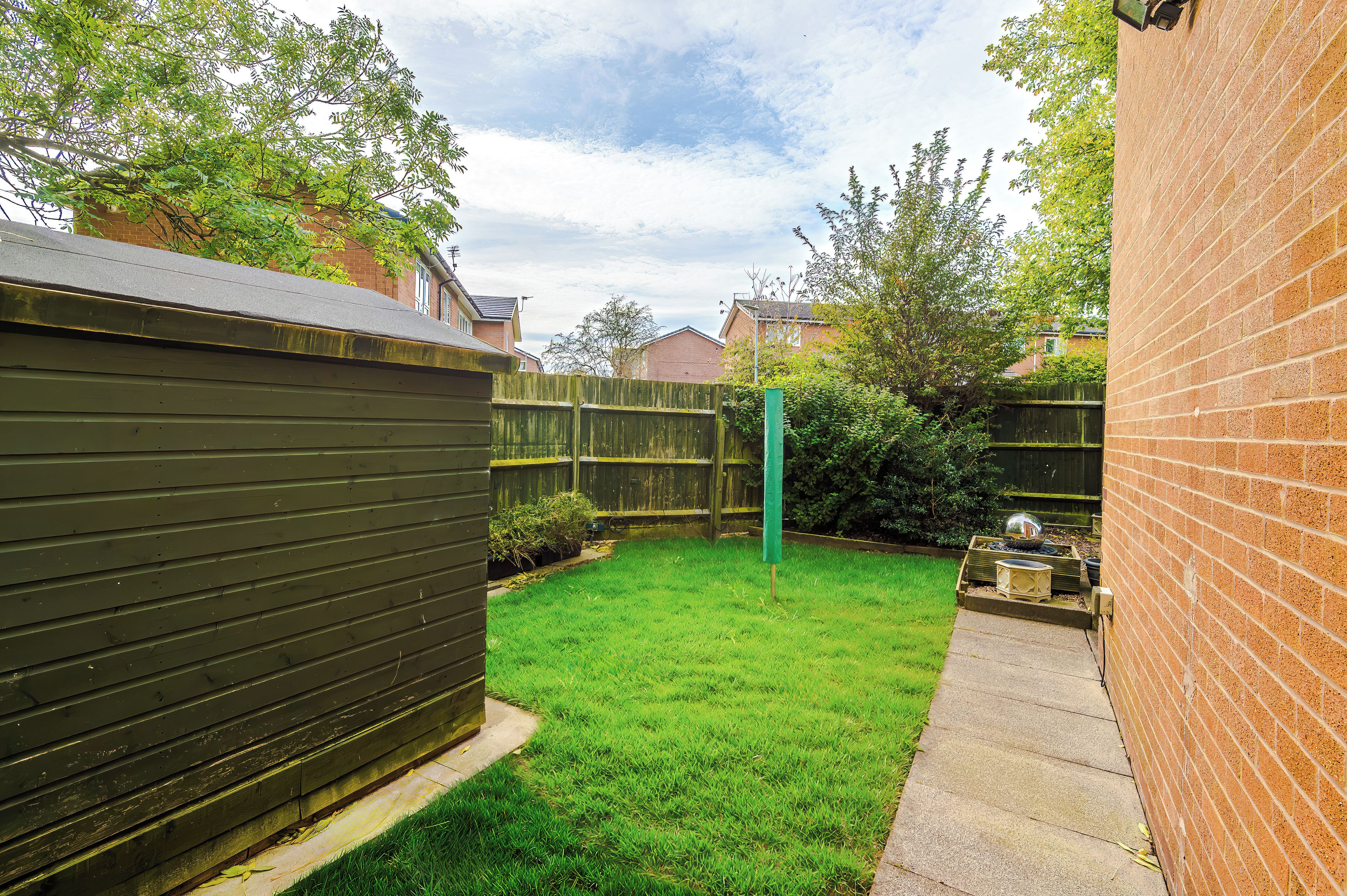 A backyard with a green lawn, a wooden fence, and a brick wall.