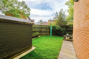 A backyard with a green lawn, a wooden fence, and a brick wall. - 3-Bed Home, Garden & Driveway, Sleeps 6 (Knutsford)