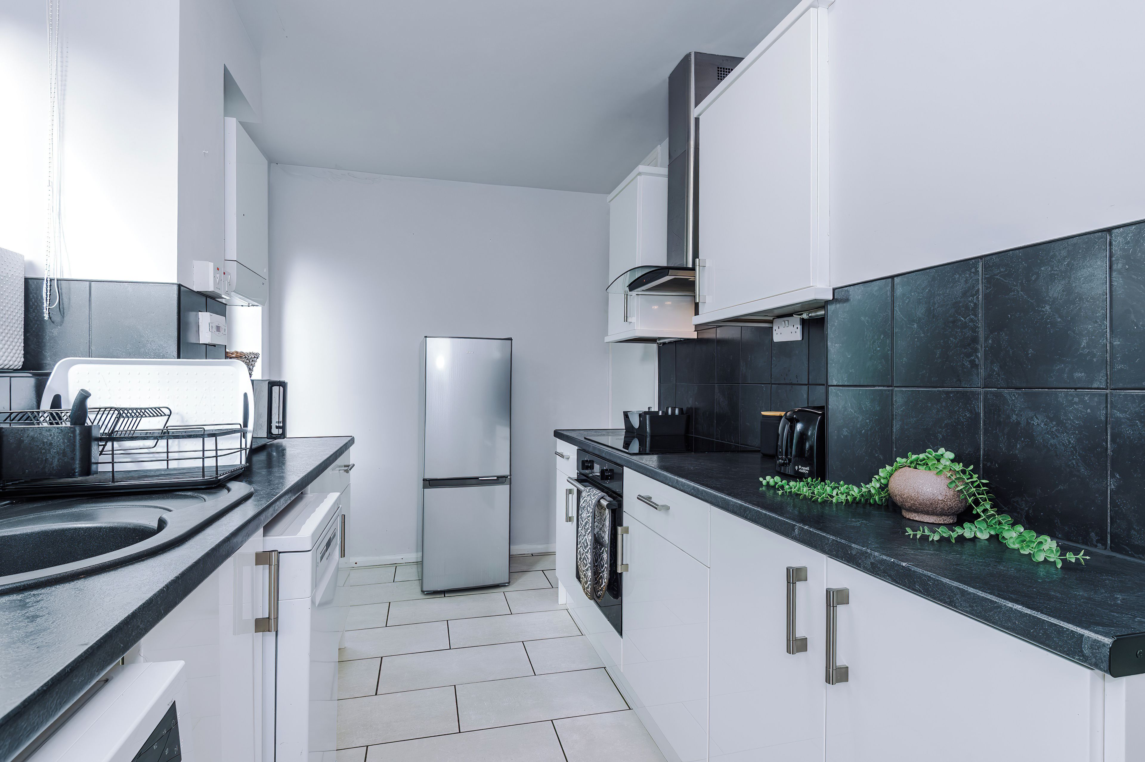 A modern kitchen with white cabinets, a stainless steel refrigerator, and a black countertop.