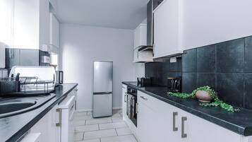 A modern kitchen with white cabinets, a stainless steel refrigerator, and a black countertop.