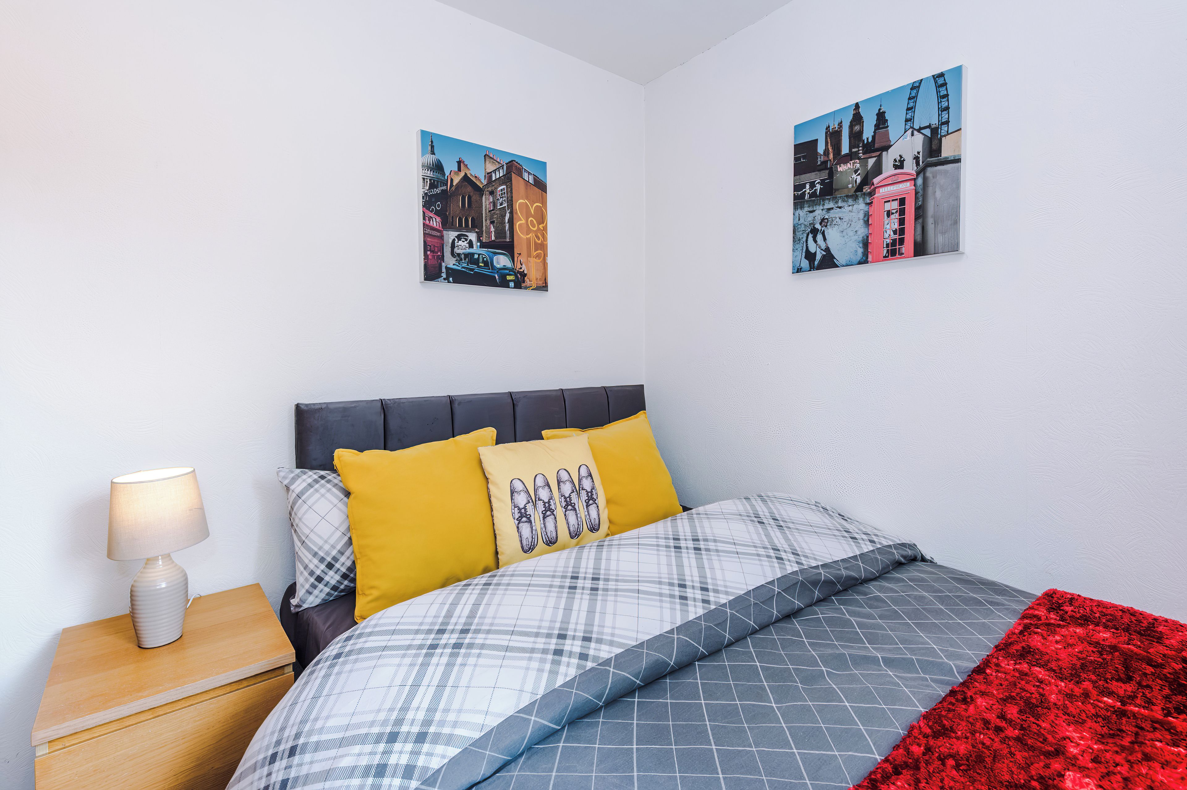A bedroom with a bed, pillows, a nightstand, a lamp, and two wall-mounted paintings.