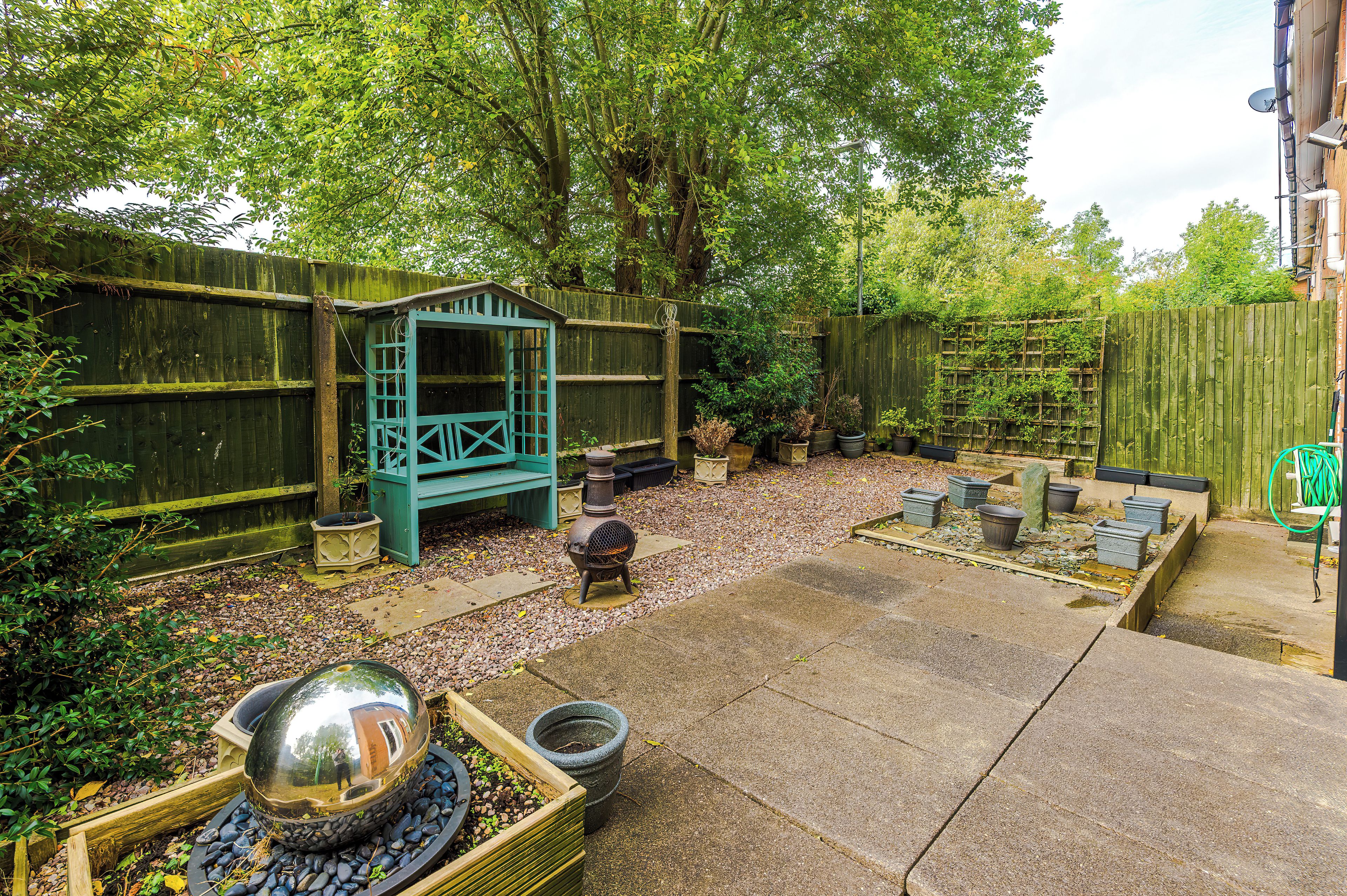 A garden with a wooden fence, a green bench, and a barbecue grill.