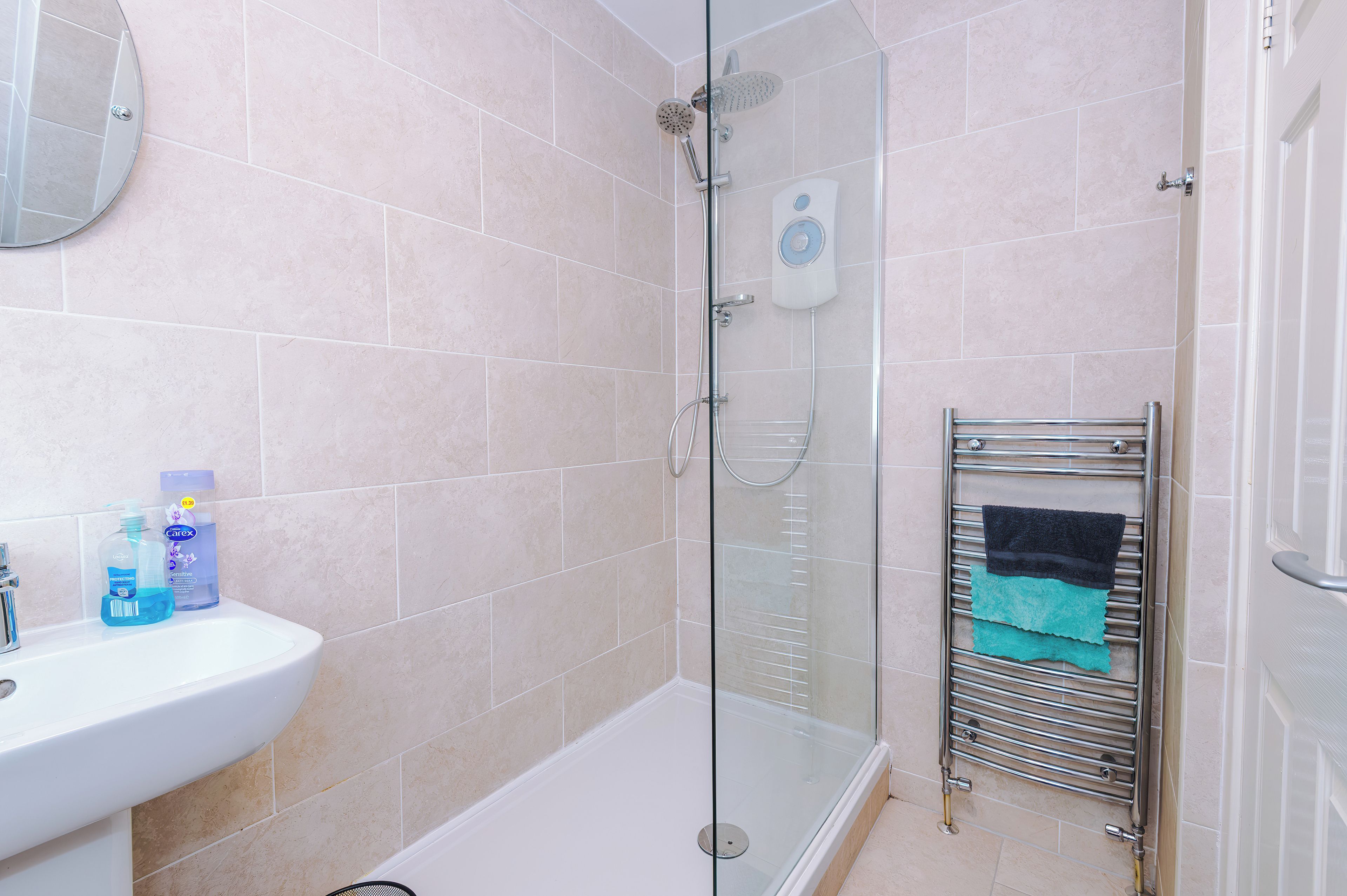 Un baño con ducha envuelta en vidrio, un lavabo blanco y un perchero para toallas.