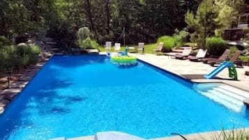 Een rechthoekig zwembad met een whirlpool voorop, omringd door een terras met ligbedden en een glijbaan.