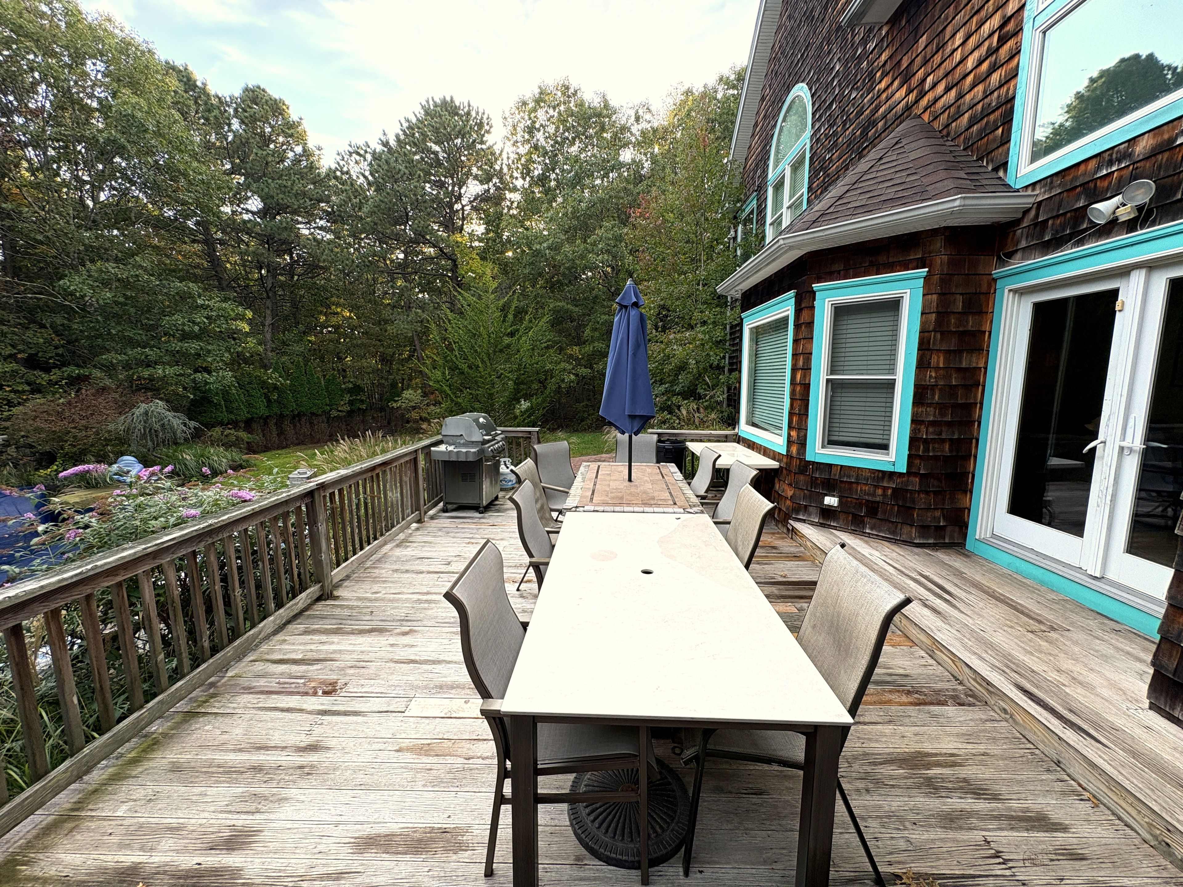 A wooden deck with a table and chairs, a grill, and a blue umbrella.