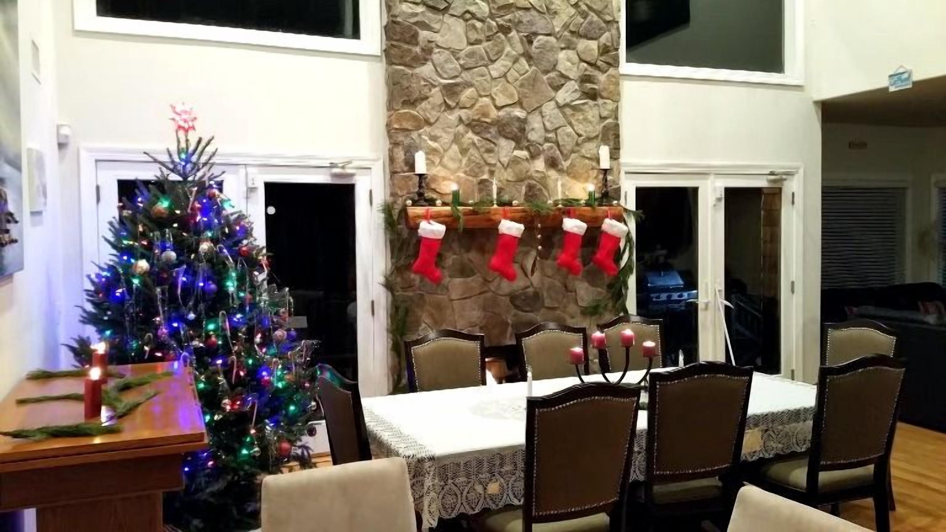 A dining area with a Christmas tree, a stone wall, and a fireplace with stockings.