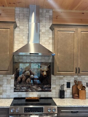 Una cocina con extractor de acero inoxidable, armarios de madera y un salpicadero con motivos de oso.