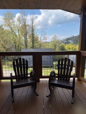 Terraza de madera con dos sillas Adirondack orientadas a una vista panorámica de árboles y una casa al fondo.