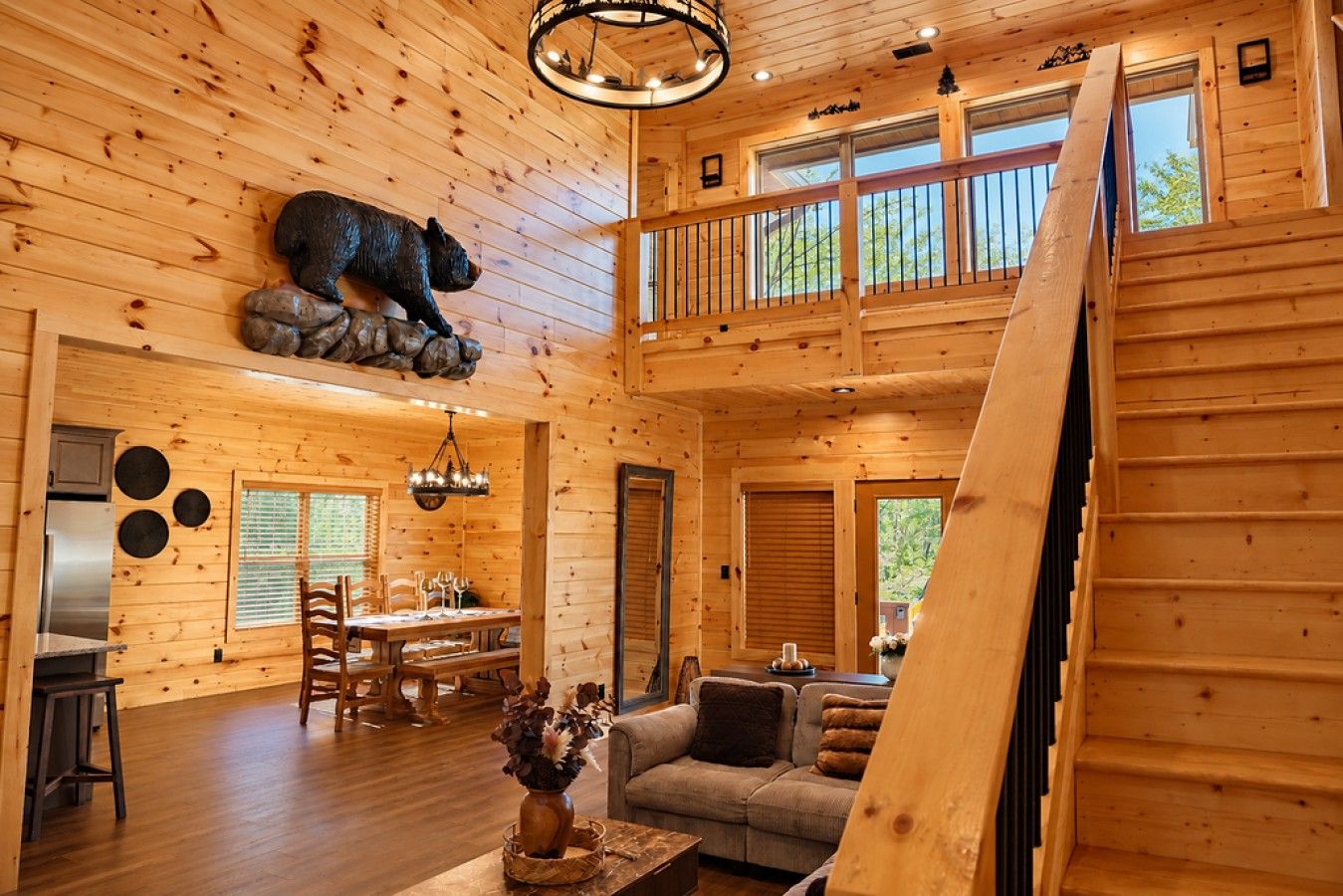 Interior de una cabaña con comedor, sofá y una escultura de oso.