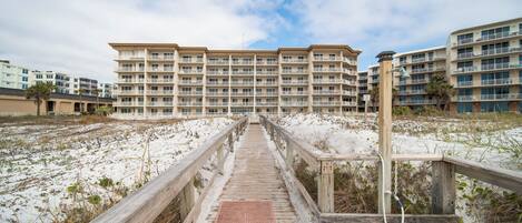 Un muelle de madera que conduce a una zona residencial frente al mar, con edificios de varios pisos.