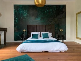 A bedroom with a large bed, a green wall tapestry, and two bedside tables with lamps.