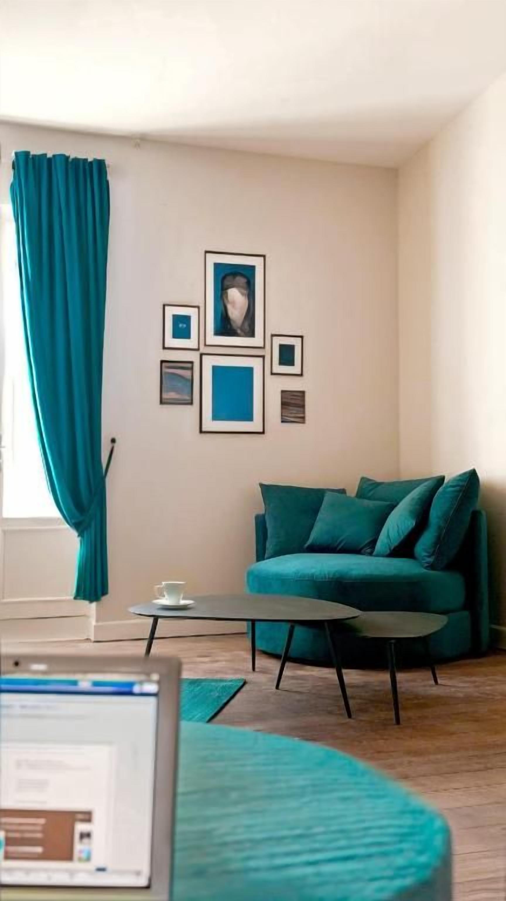 A living room with a teal sofa, a coffee table, and a laptop on a desk.