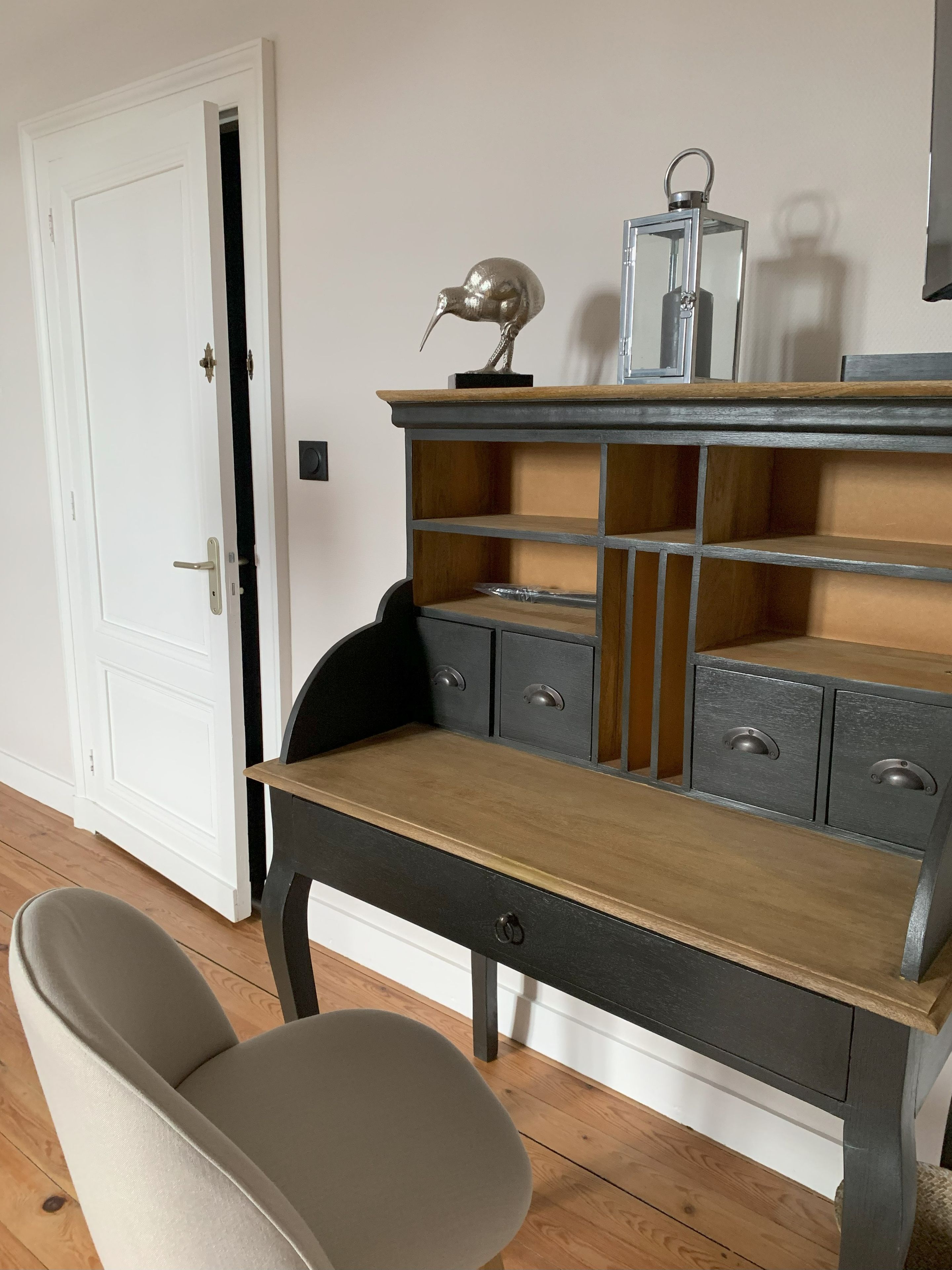 Un bureau avec des tiroirs et une étagère, une chaise et une porte en arrière-plan.