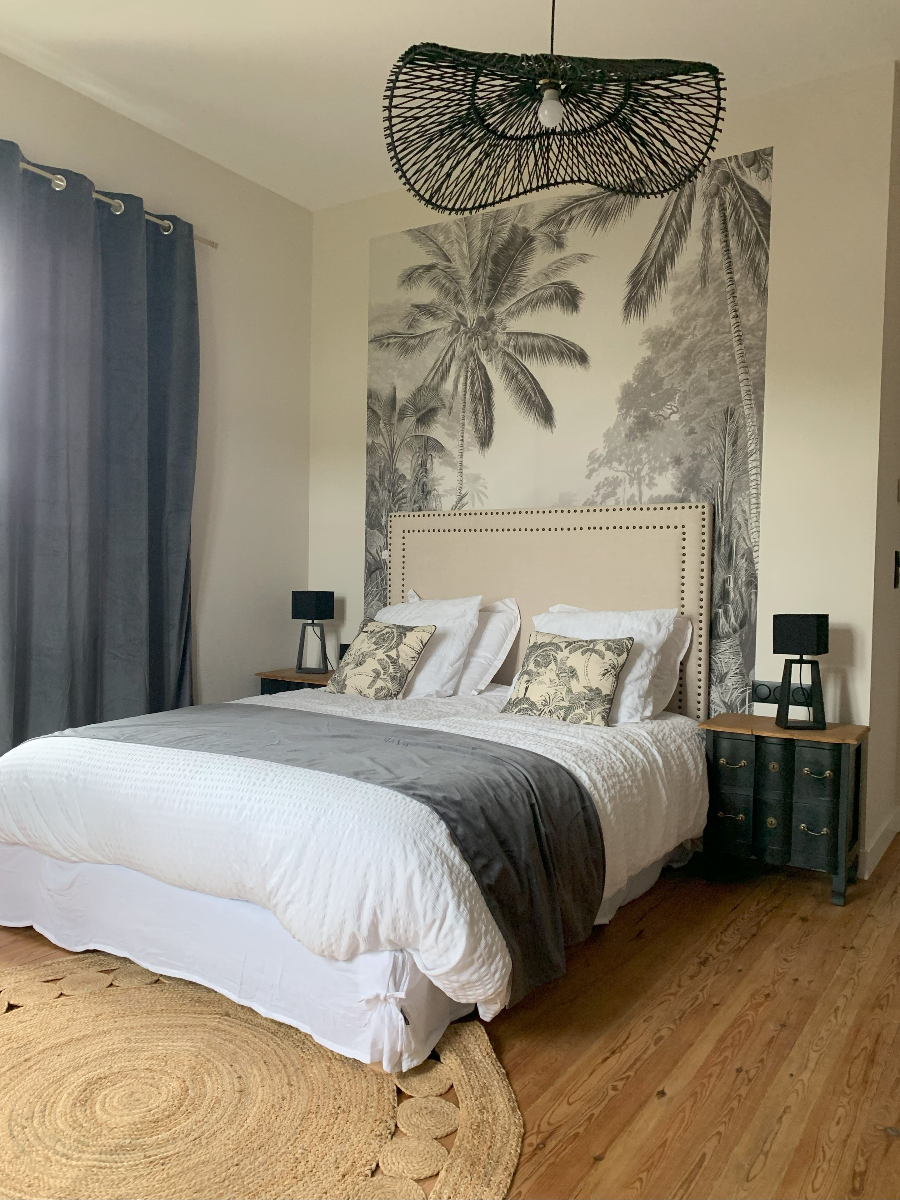 A bedroom with a bed, a wall mural, a hanging light fixture, and a nightstand.