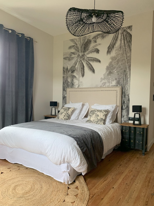 A bedroom with a bed, a wall mural, a hanging light fixture, and a nightstand.