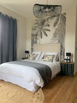 A bedroom with a bed, a wall mural, a hanging light fixture, and a nightstand.