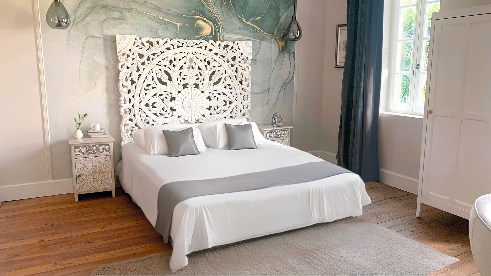 A bedroom with a bed, nightstands, a decorative headboard, a window with curtains, and a door.