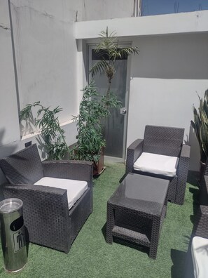 Un patio en la azotea con mobiliario de mimbre, una planta en maceta y una puerta.
