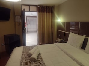 Habitació d'hotel amb un llit, una taula de nit amb un telèfon, una televisió penjada a la paret i una porta que dóna al passadís.