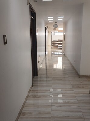 A hallway with a shiny tiled floor, a door on the left, and a staircase at the end.