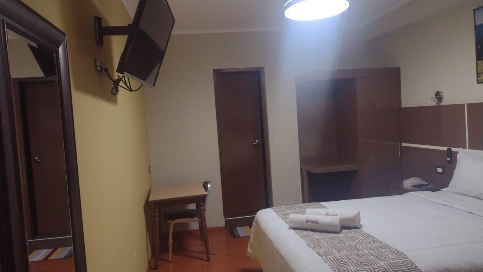 Una habitación de hotel con cama, escritorio, silla, televisor y puerta.
