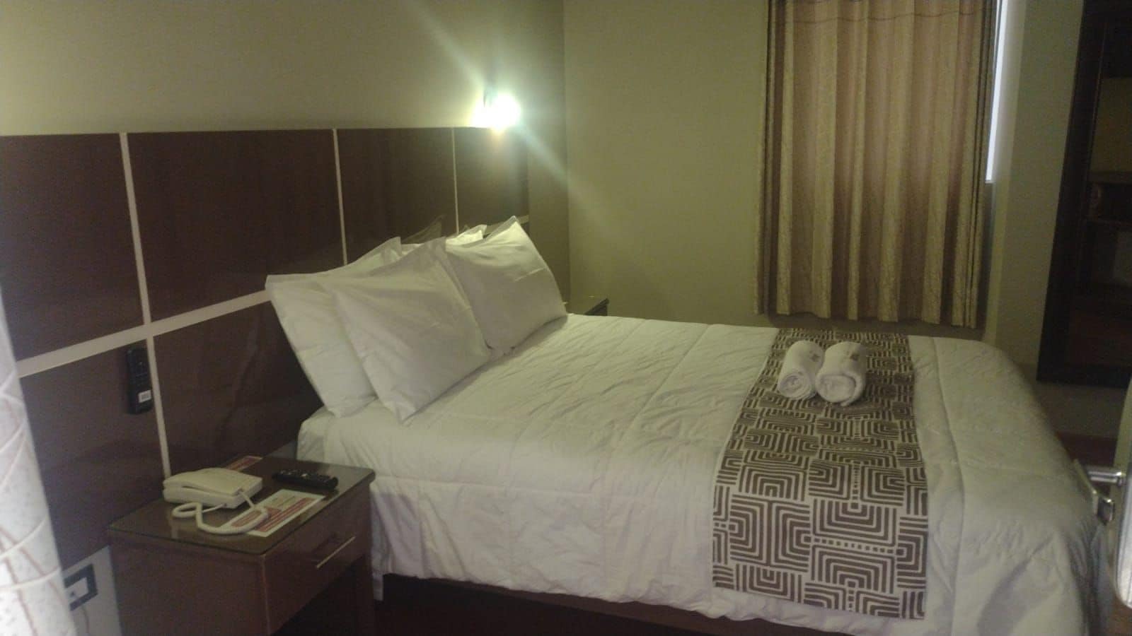 Una habitación de hotel con una cama, una mesita de noche con un teléfono y una manta decorativa.