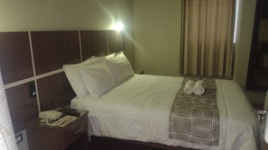 Habitació d'hotel amb un llit, una taula de nit amb un telèfon i una manta decorativa.