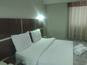 Habitació d'hotel amb llit, almoinades, una tauleta de nit, làmpada i finestra amb cortines.