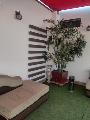 Una habitación con un sofá, una planta en maceta, un bote de basura y un estante fijado a la pared.
