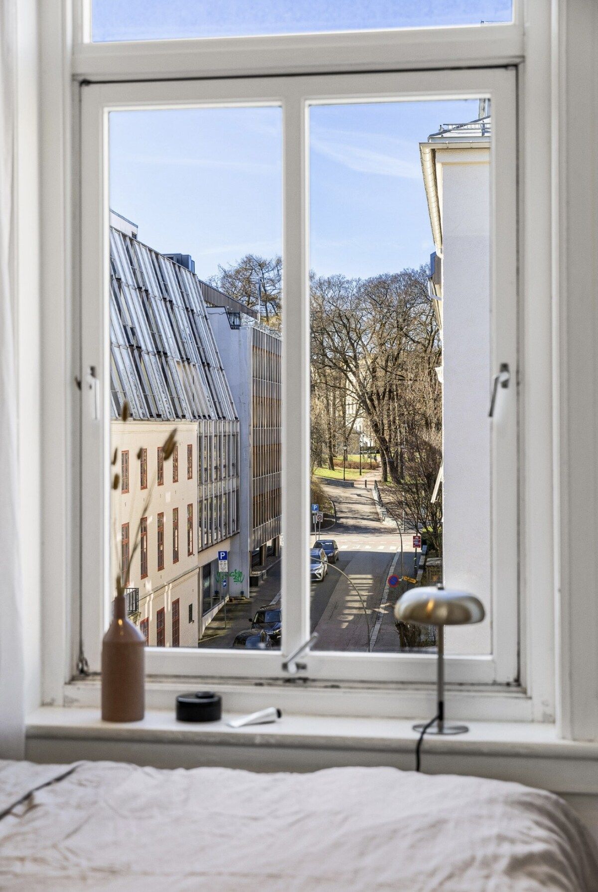 A room with a large window overlooking a street with buildings and trees.