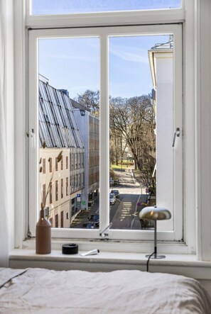 Ein Zimmer mit großem Fenster und Blick auf eine Straße mit Gebäuden und Bäumen.